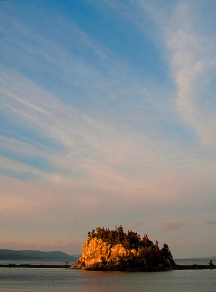 The setting sun casts an orange hue on this limestone island while turning the clouds in the sky a pinkish purple; views like this abound on Nova Scotia’s Cabot Trail.