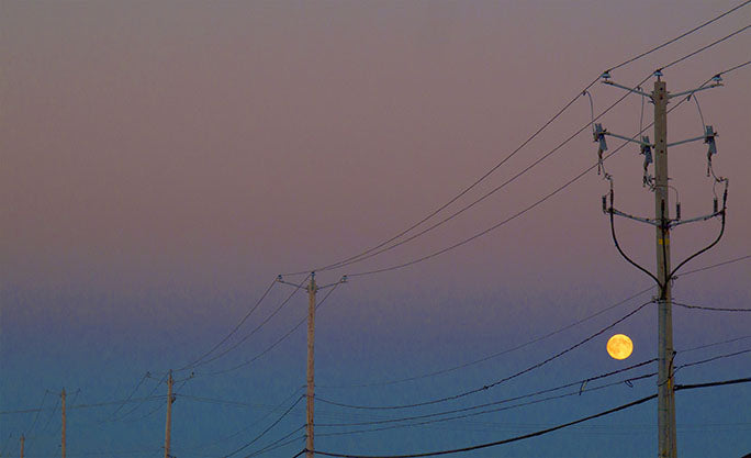 While riding his 1995 Honda Shadow VT100 motorcycle through Amos, Quebec in search of somewhere to stay for the night, photographer Geoffrey Kula captured this image of the full moon framed by powerlines.